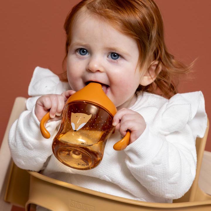 Baby holding and drinking from a Trixie Tritan sippy cup with a fun animal design of Mr. Fox.